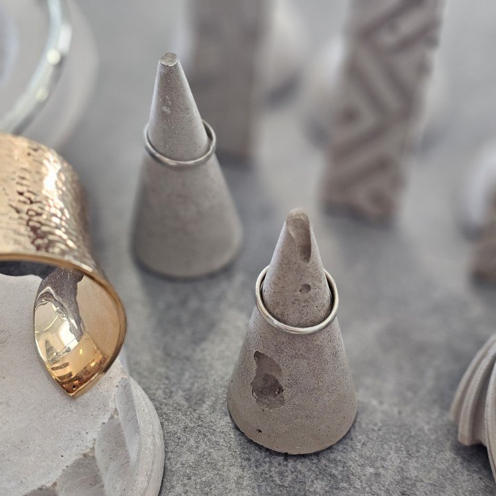 Two cone-shaped concrete ring holders next to a gold cuff bracelet